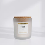 White soy candle in frosted vessel with cork lid. "Bloom" is in black on label with "limited edition" in gold. White background