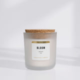 White soy candle in frosted vessel with cork lid. "Bloom" is in black on label with "limited edition" in gold. White background